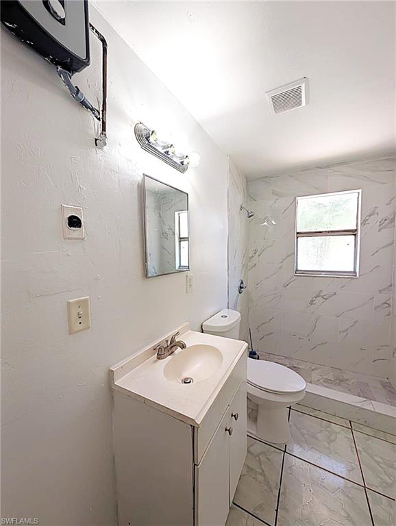 Bathroom featuring a single vanity, a toilet, a shower, a window, and an exhaust fan