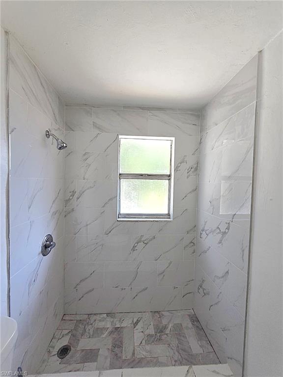 Walk-in shower with full-height white marble-look tile walls, a frosted window, and a herringbone-patterned floor