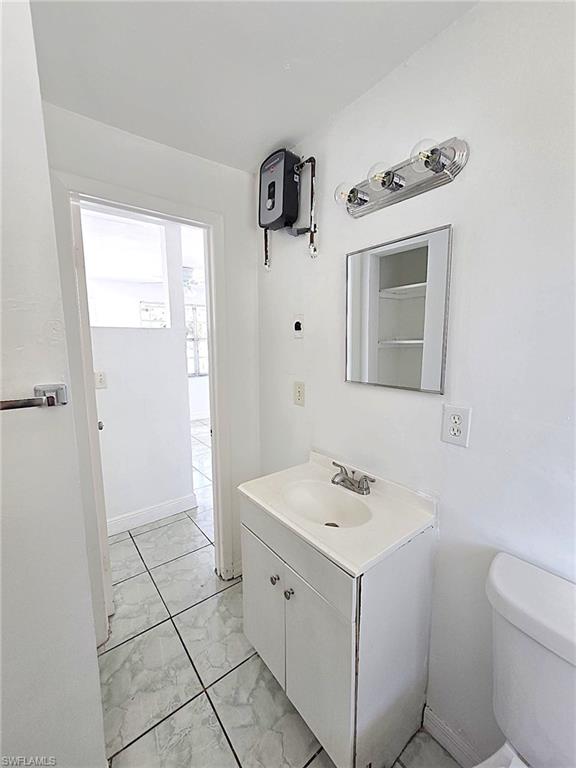 Bathroom featuring a white vanity with integrated sink, chrome faucet, wall-mounted mirror, three-bulb vanity light, and tiled flooring