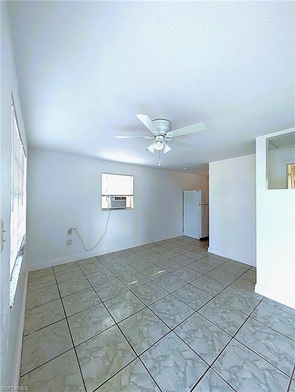 Spacious room featuring large format tile flooring, a window-mounted air conditioning unit, and a ceiling fan with integrated lighting