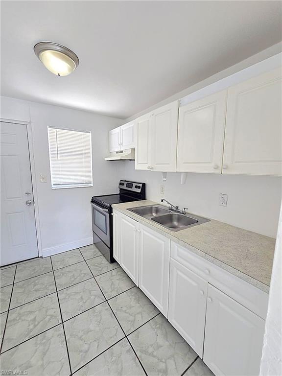 Kitchen featuring an electric range, dual basin stainless steel sink, white cabinetry, and light-toned countertops