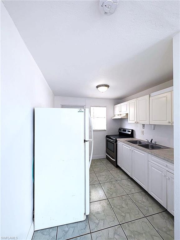 Kitchen featuring white cabinetry, a dual-basin stainless steel sink, black electric range, and a white refrigerator