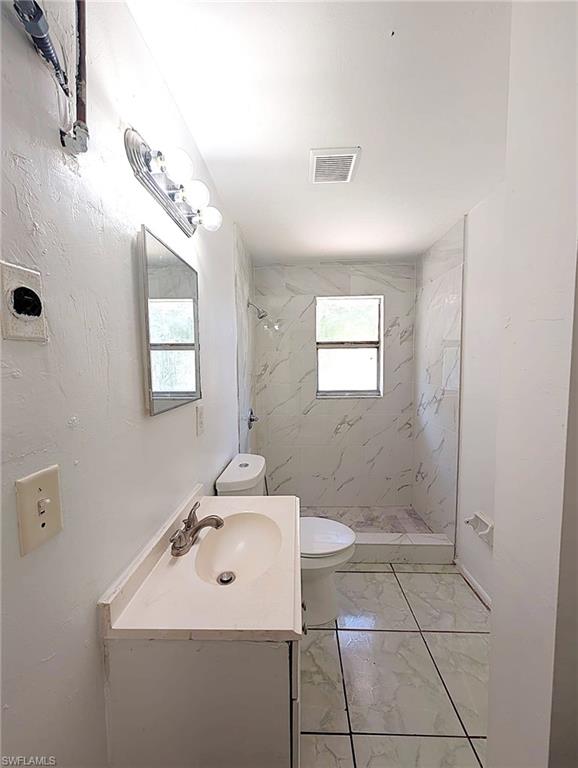 Bathroom featuring a white vanity with integrated sink, a wall-mounted mirror, a toilet, a shower with white and grey patterned wall tiles, and patterned floor tiles