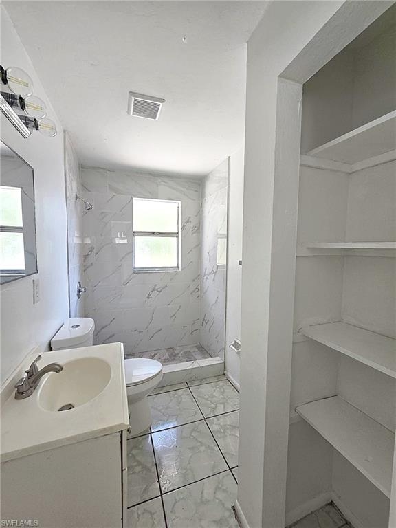 Bathroom featuring a walk-in shower with marble-look tile surround, a single vanity with an integrated sink, and built-in shelving