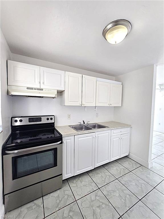 Kitchen featuring white shaker-style cabinetry, a stainless steel electric range, a double basin sink, and light-toned countertops