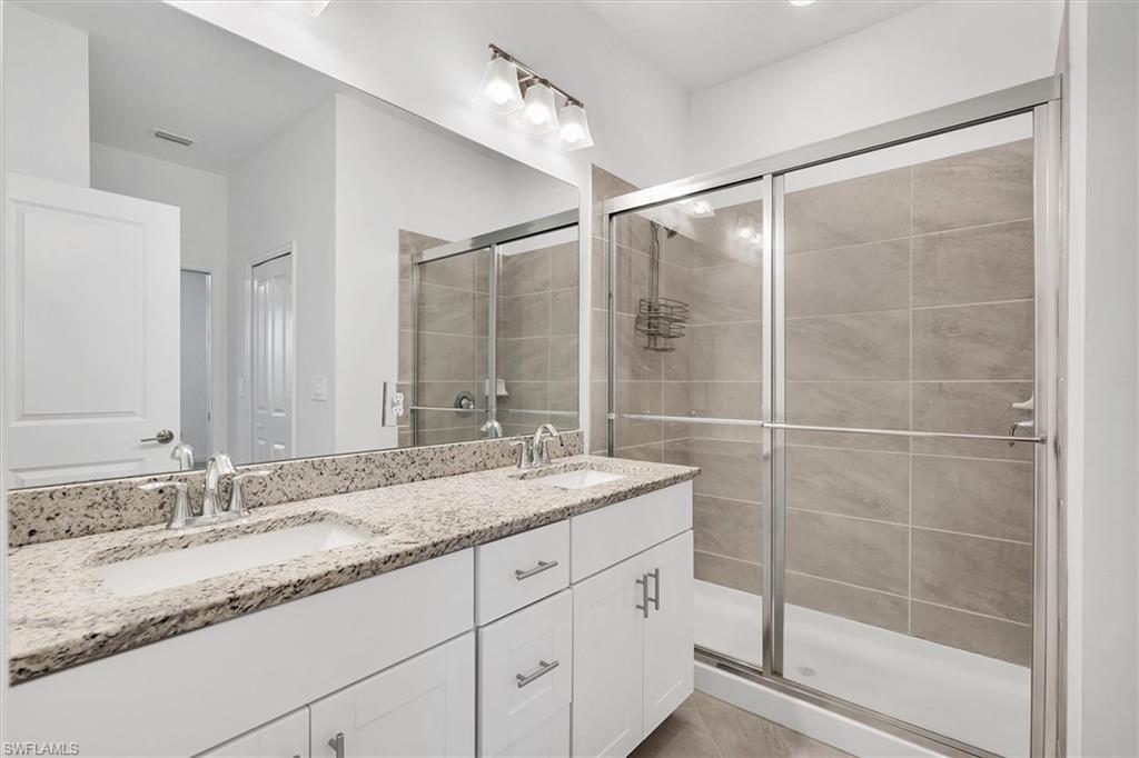 Bathroom with a shower stall, double vanity, and light tile patterned flooring