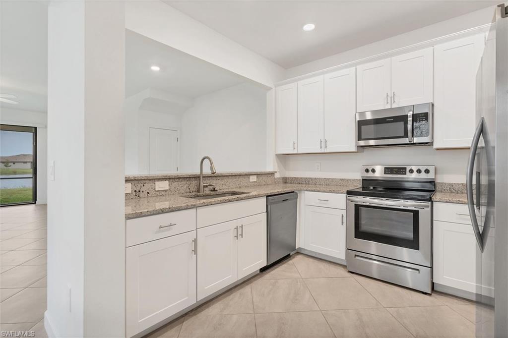 Kitchen with appliances with stainless steel finishes, light stone counters, white cabinetry, light tile patterned floors, and recessed lighting