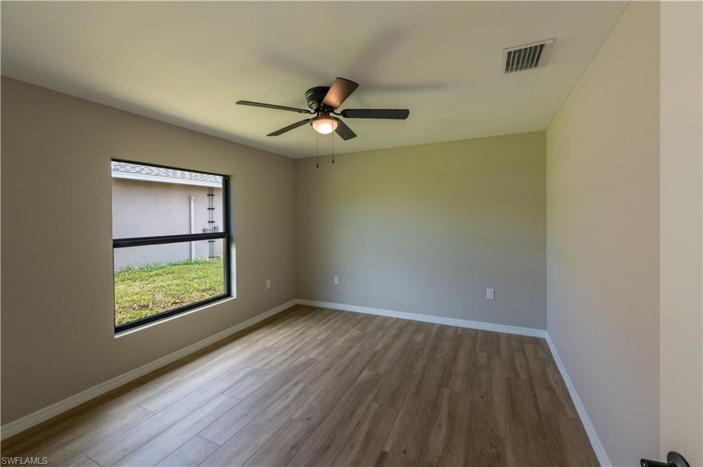 Neutral wall color, wood-finish flooring, ceiling fan with integrated lighting, and a window with black trim