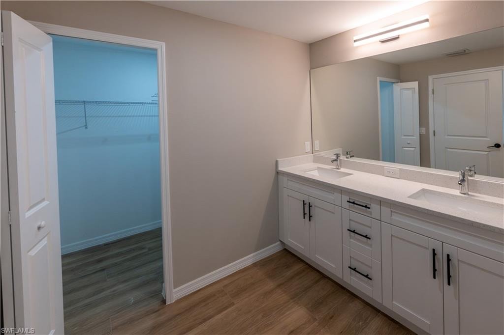 Dual vanity with white cabinetry and black hardware, stone-finish countertop, and full-width mirror