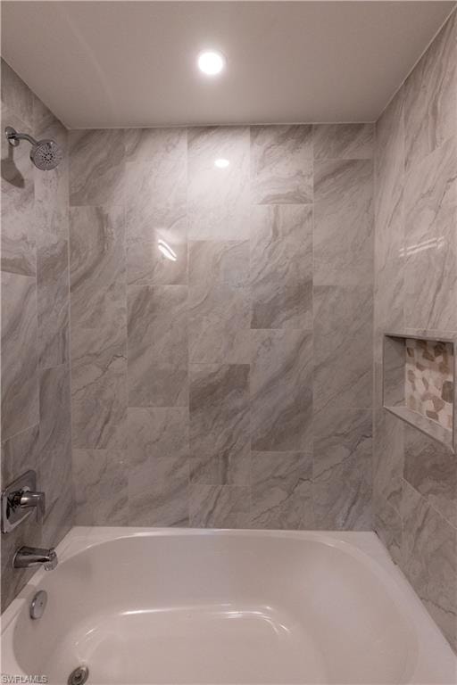 Bathtub with a chrome showerhead and faucet, surrounded by tiled walls featuring a mosaic-tiled inset niche