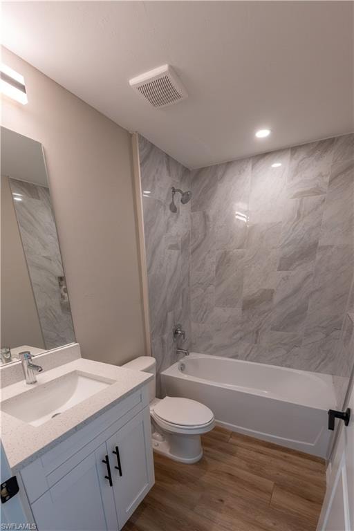 White vanity with a light-colored countertop and integrated sink, chrome faucet, wood-finish flooring, and a white bathtub with large format grey-patterned wall tiles