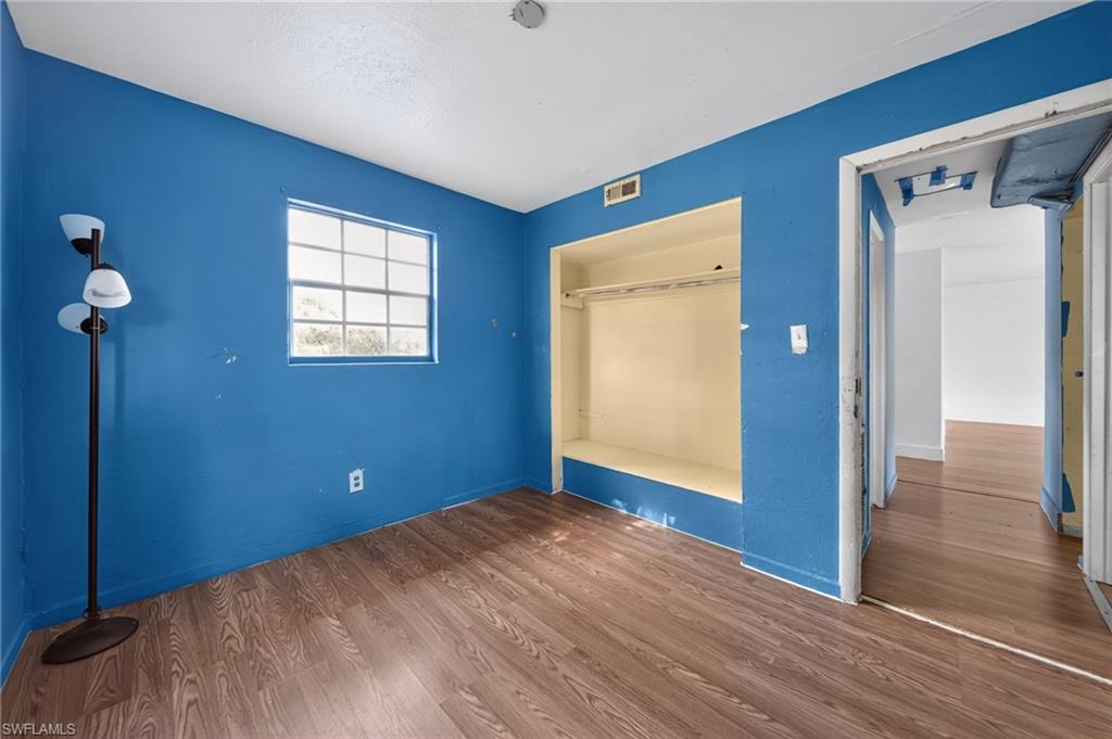 Wood-finish flooring throughout, featuring a built-in closet with shelving and a hanging rod, a window with exterior views, and a white ceiling