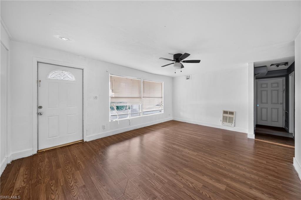 Spacious room featuring wood-finish flooring, white walls, and a ceiling fan with integrated lighting