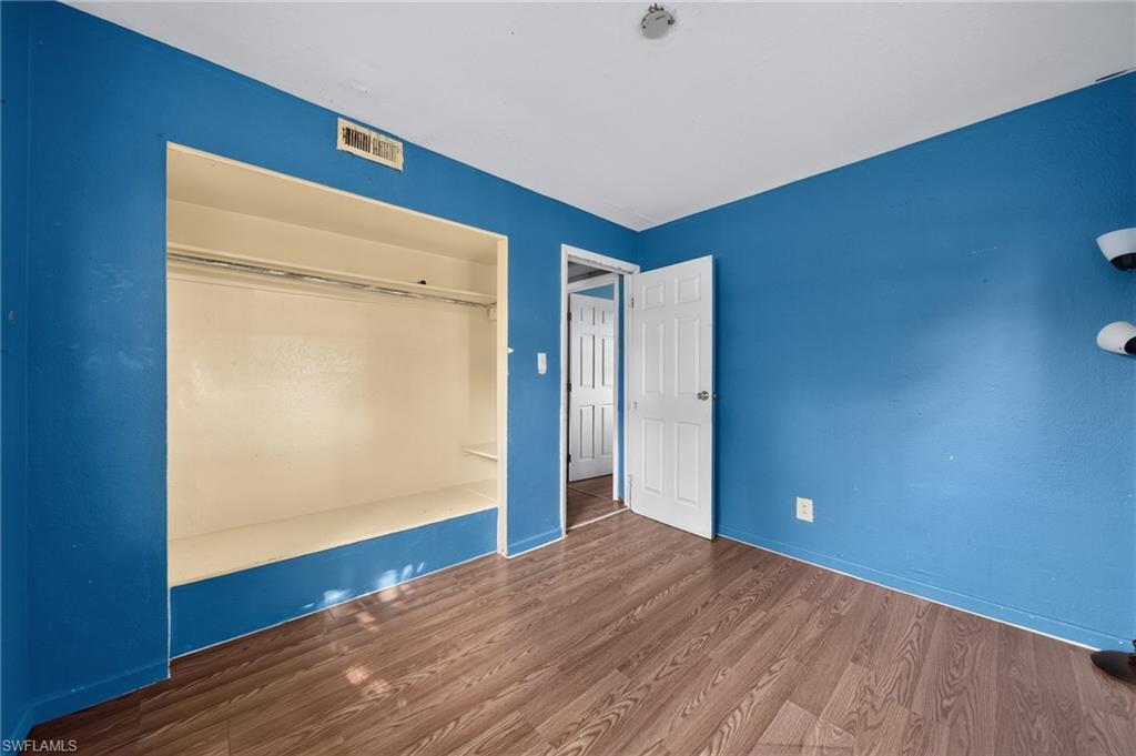 Room featuring wood-finish flooring, vibrant blue walls, a white ceiling, and a built-in closet with shelving and a hanging rod