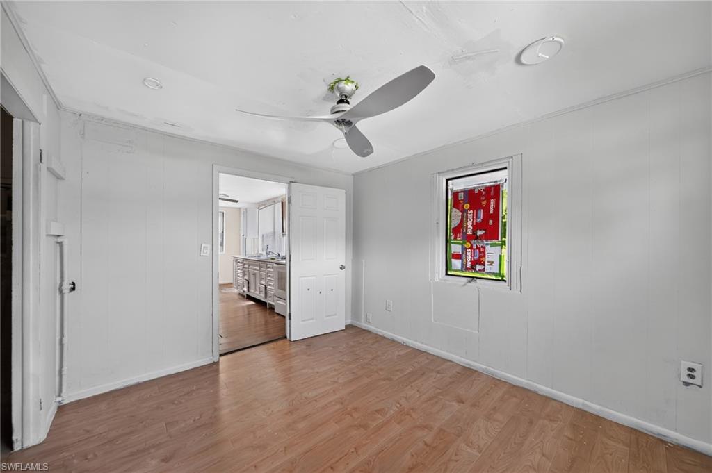 Spacious room featuring wood-finish flooring, white panel walls, and a ceiling fan with integrated lighting
