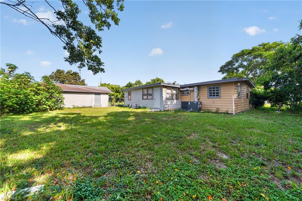 Expansive rear yard featuring green lawn space, a detached structure with a metal door, and a single-story residence with horizontal siding and a window unit
