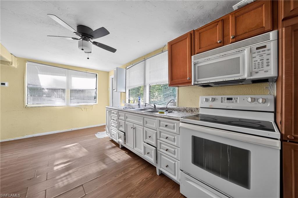 Kitchen featuring wood-finish flooring, white cabinetry with silver hardware, a white electric range, and an over-the-range microwave