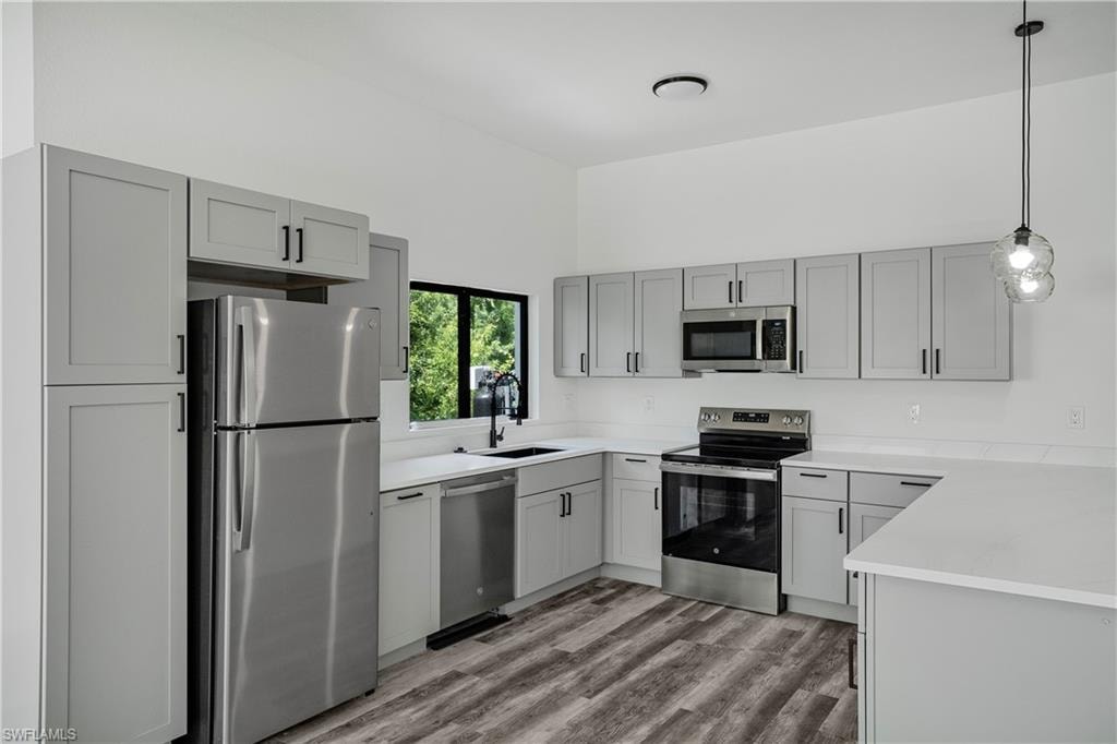 Modern kitchen featuring light gray cabinetry with black hardware, stainless steel appliances, white countertops, and wood-finish flooring