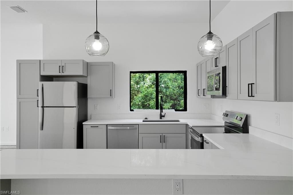 Bright kitchen with light gray cabinetry, stainless steel appliances, and white countertops