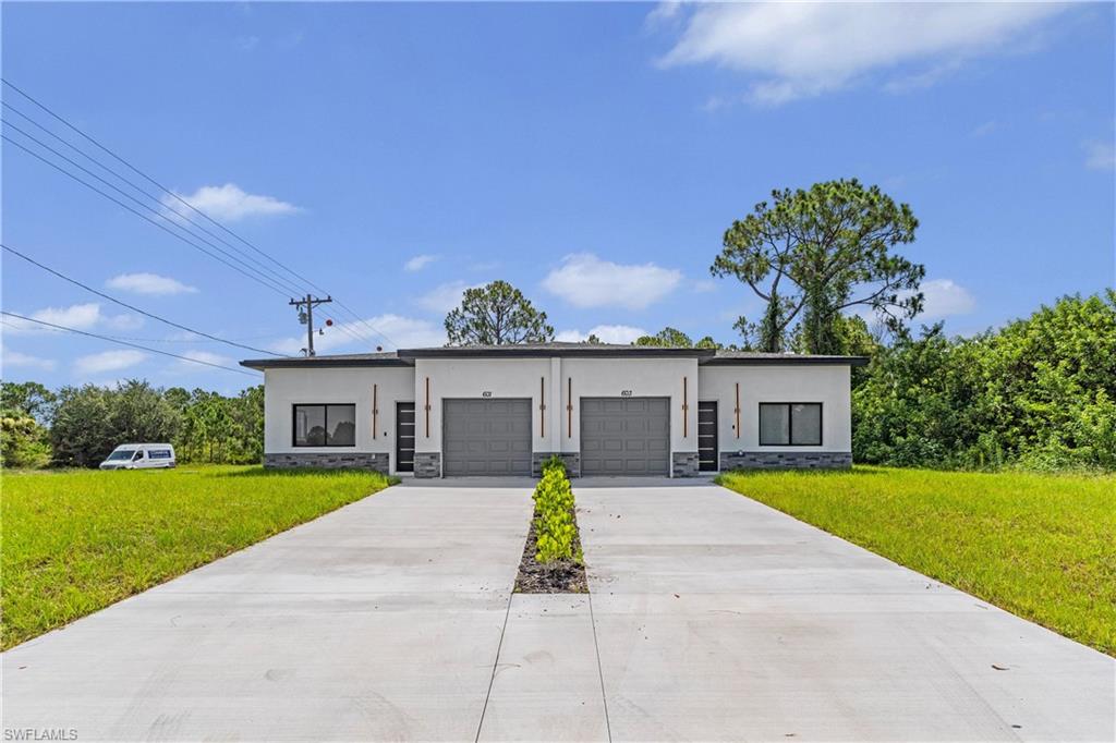 Modern duplex property featuring a clean stucco exterior, stone veneer accents, individual garage doors, contemporary entrance doors with vertical glass inserts, and a shared concrete driveway