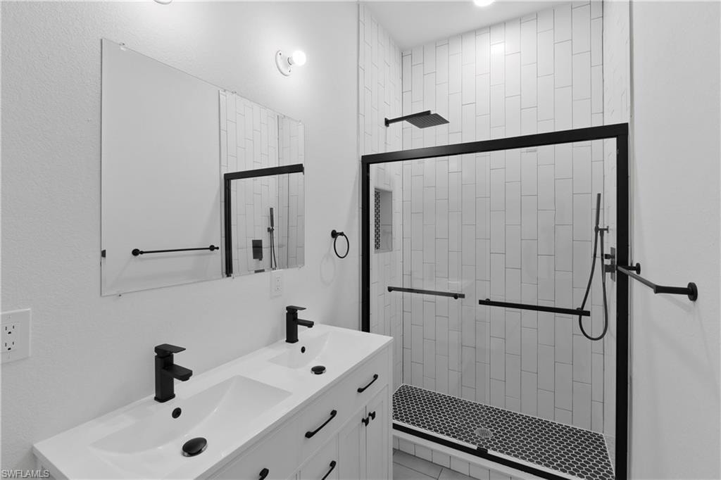 Modern bathroom featuring a dual-sink vanity with matte black fixtures, a contemporary walk-in shower with subway tile surround, a built-in shower niche, a rain shower head, and a handheld shower unit