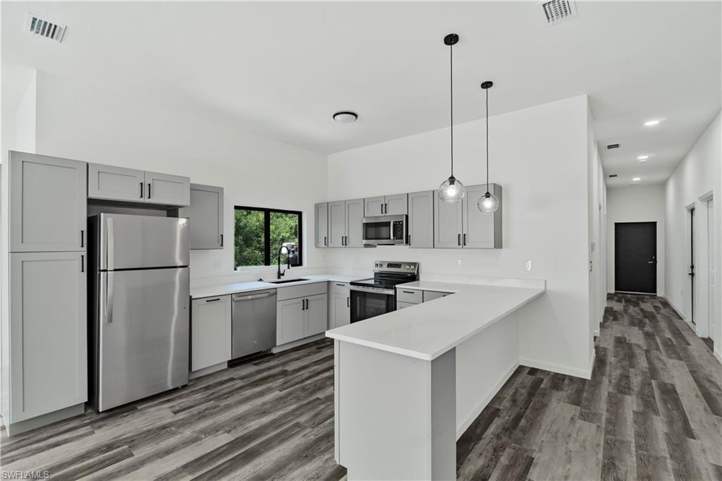 Open-concept kitchen featuring gray shaker cabinetry, stainless steel appliances, white countertops, and wood-finish flooring