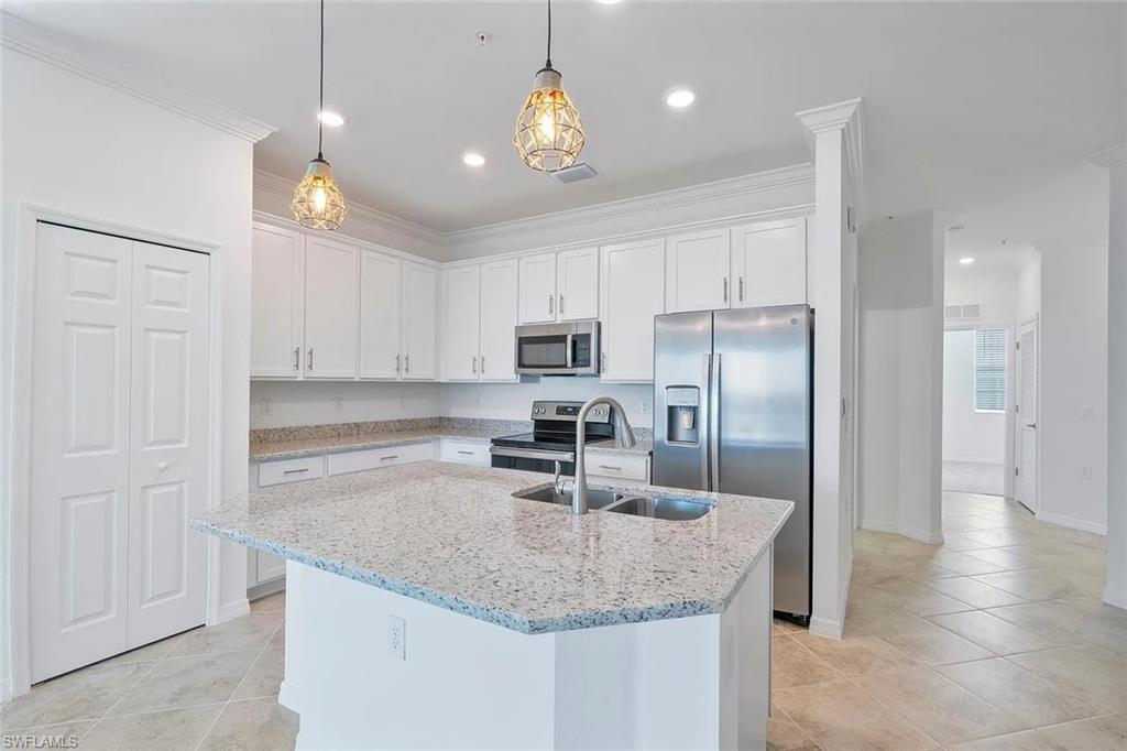 Modern kitchen featuring white cabinetry, light-toned stone countertops, stainless steel appliances, and a central island with an undermount double basin sink