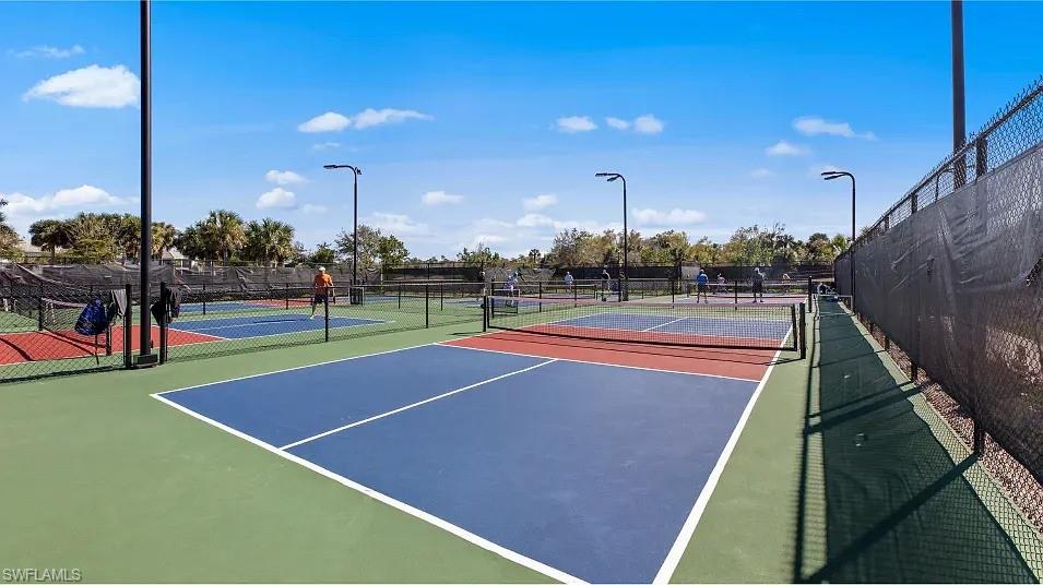 Multiple pickleball courts featuring blue and red playing surfaces, green surrounds, and perimeter fencing