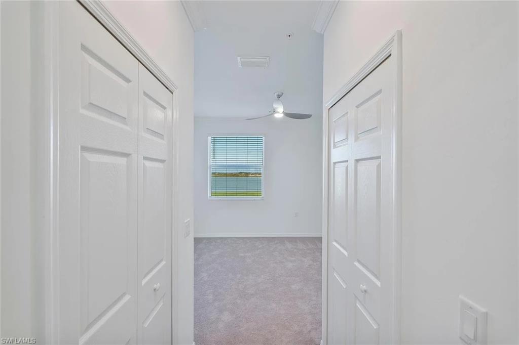 Interior hallway featuring bi-fold panel doors and light gray carpeting leading to a room with vaulted ceilings, a window with horizontal blinds, and a ceiling fan