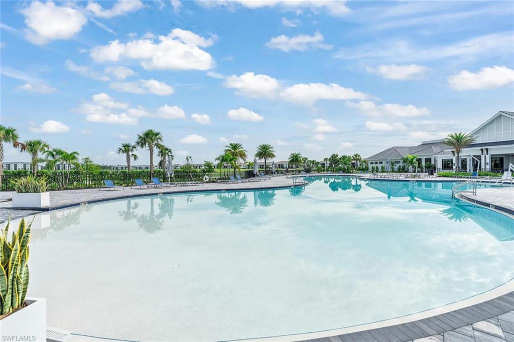 Expansive resort-style swimming pool featuring a large deck, multiple lounge chairs, and surrounding palm trees
