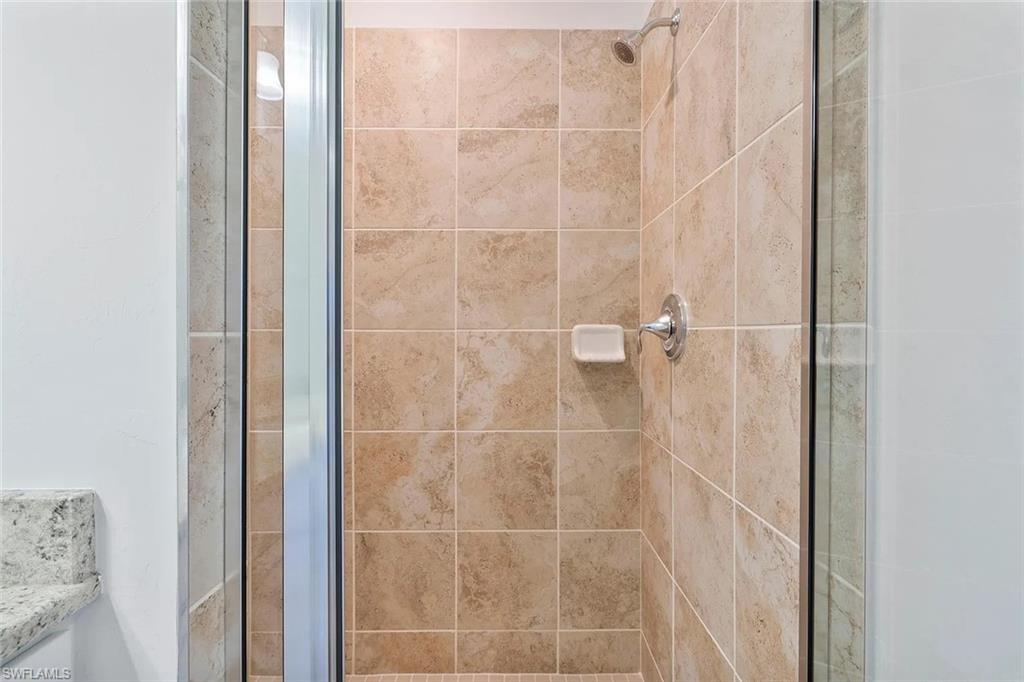 Shower enclosure featuring neutral-toned square tile, chrome fixtures, and a glass door