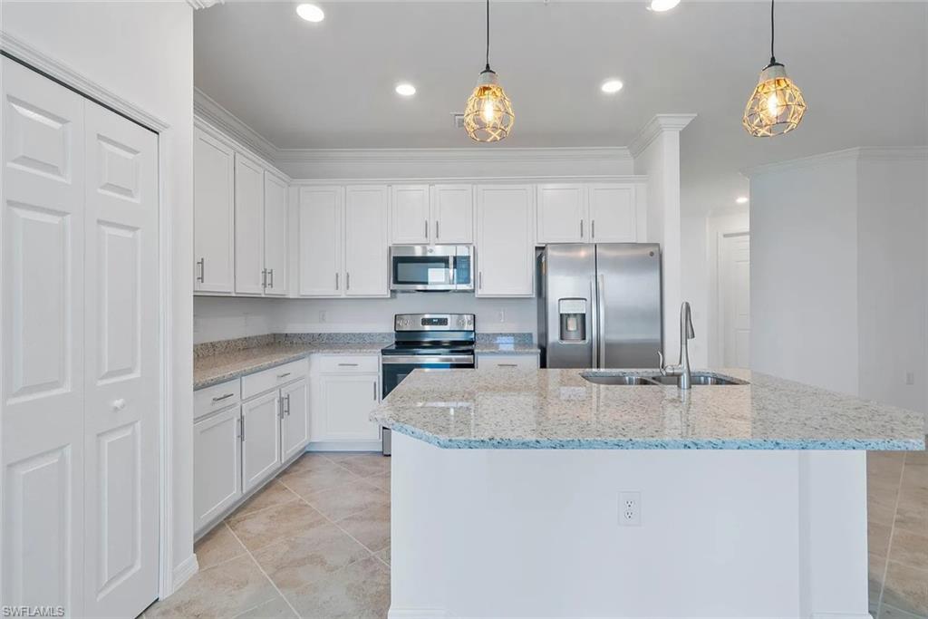 White kitchen featuring granite countertops, stainless steel appliances, a center island with sink, contemporary pendant lighting, and tiled flooring
