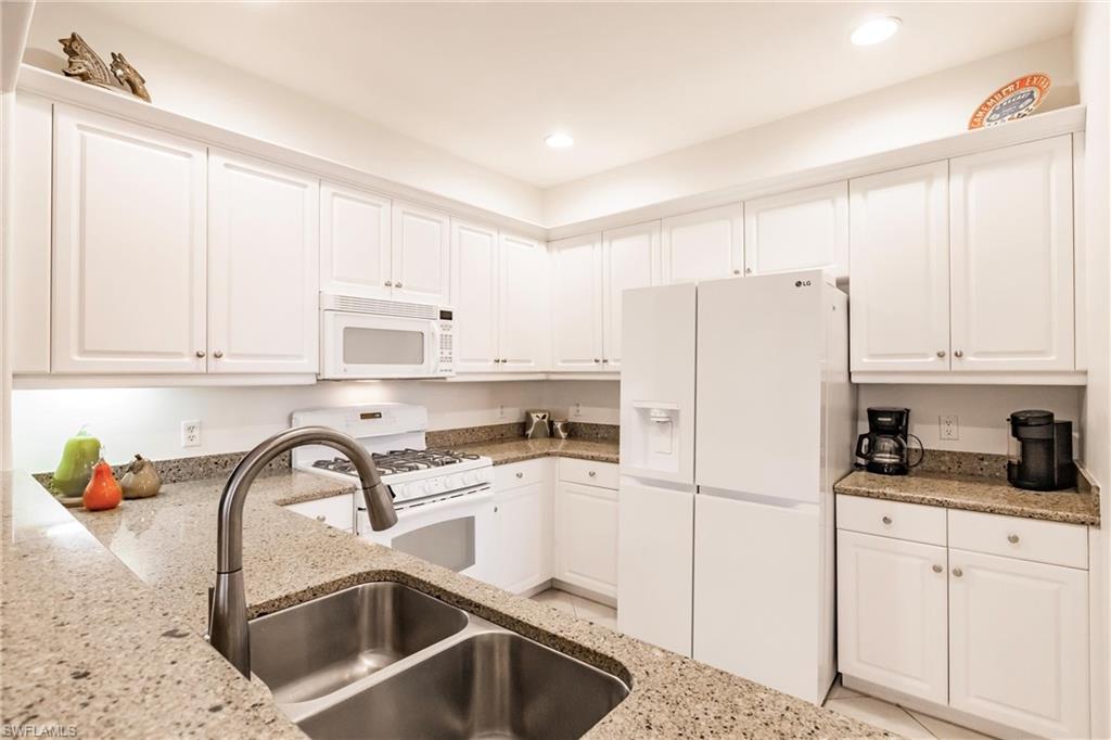 Kitchen featuring white cabinetry, white appliances, light stone counters, and recessed lighting