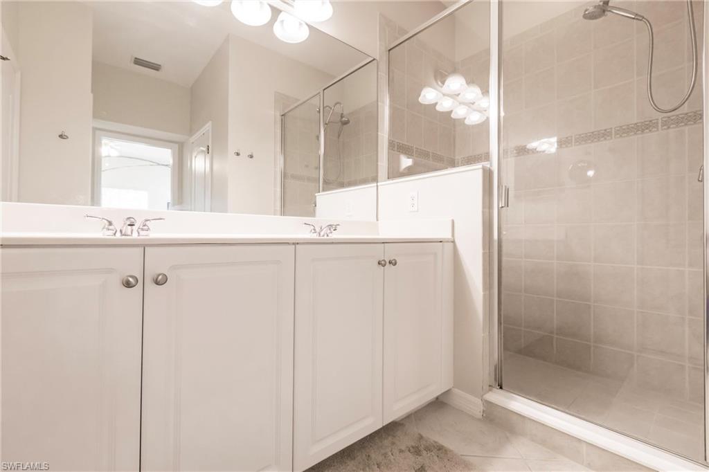 Bathroom with double vanity, a shower stall, and light tile patterned floors