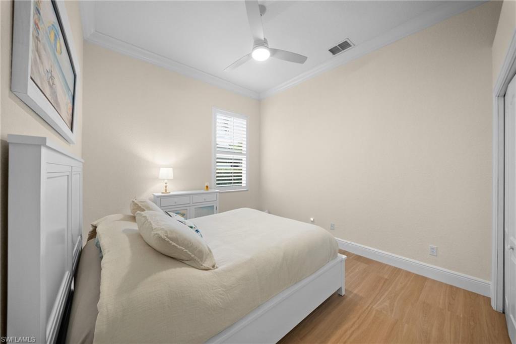 Bedroom featuring wood-finish flooring, a vaulted ceiling with a ceiling fan, crown molding, and a window with plantation shutters