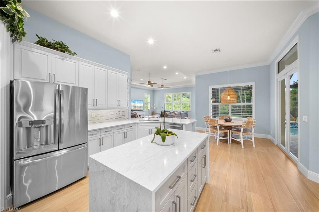 Modern kitchen featuring a large center island with a stone-finish countertop, white cabinetry, stainless steel appliances, and wood-finish flooring