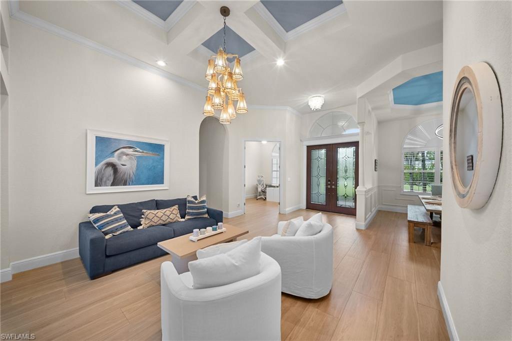Spacious living area featuring light wood-finish flooring, a coffered ceiling with a blue accent panel, and a prominent multi-tier chandelier