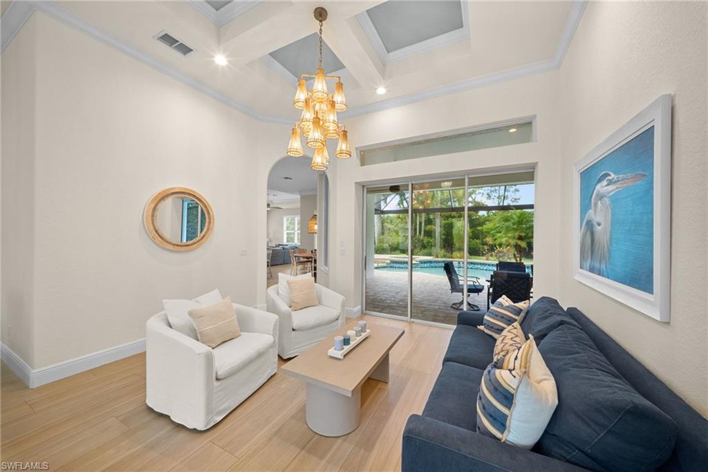 Living space featuring wood-finish flooring, a coffered ceiling with a central chandelier, and a transom window