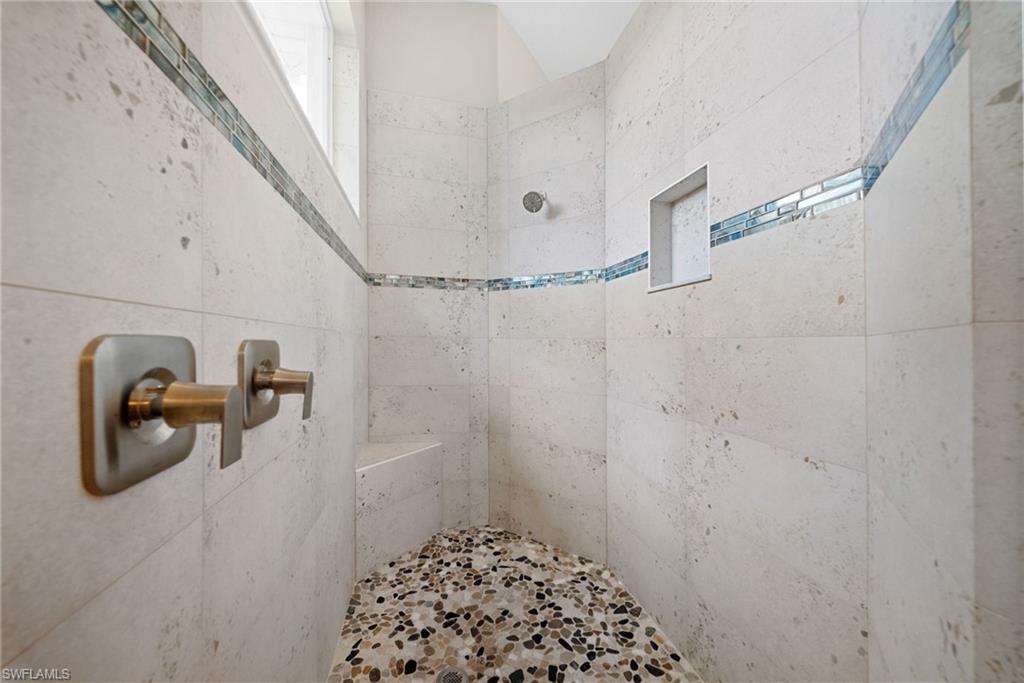 Tiled shower featuring a built-in bench with pebble flooring, light-toned wall tiles, a mosaic accent band, and a recessed shower niche