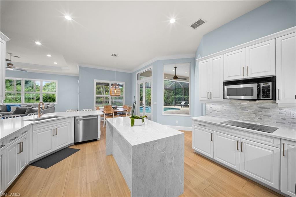 Modern kitchen featuring white cabinetry, light-toned wood-finish flooring, a central island with a waterfall countertop, integrated stainless steel appliances, and a tiled backsplash