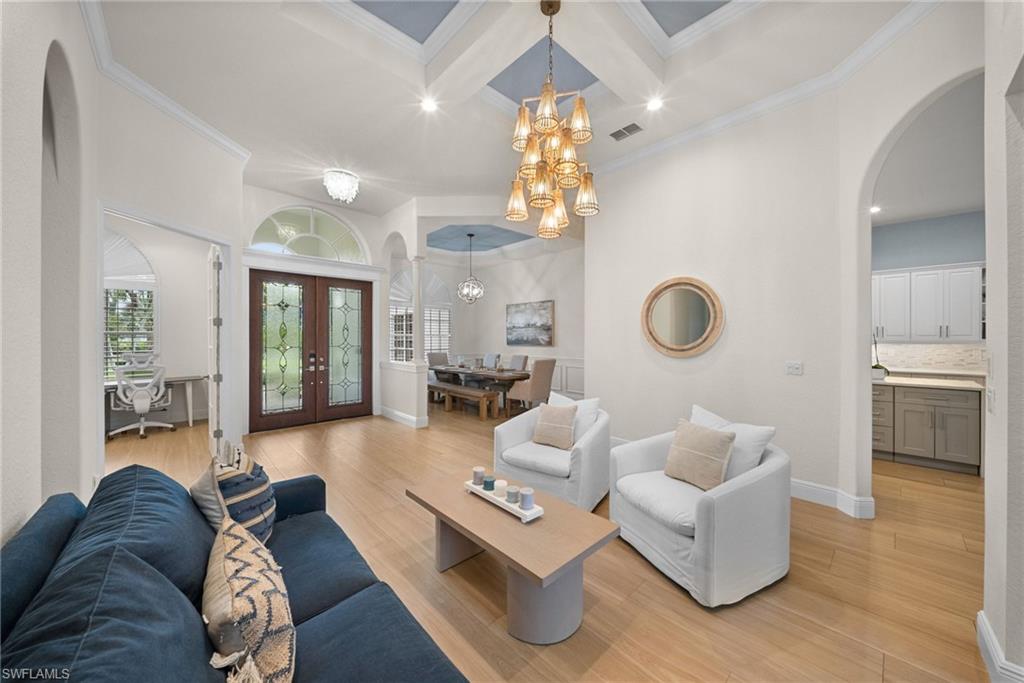 Open-concept living space with light wood-finish flooring, a tray ceiling featuring a central chandelier, recessed lighting, and crown molding