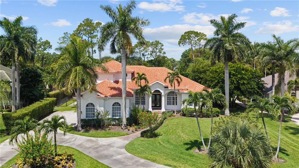Exterior featuring a terracotta tile roof, white stucco facade, arched windows, and a paved circular driveway