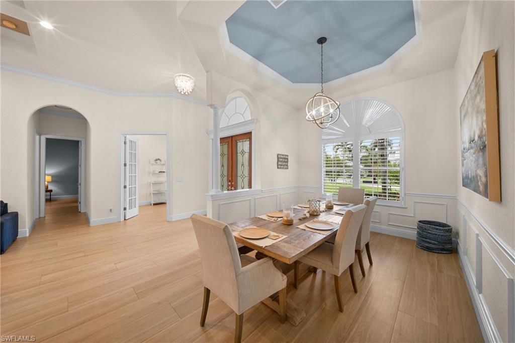 Dining area featuring wood-finish flooring, wainscoting, an arched window with plantation shutters, a coffered ceiling with a painted inset, and a contemporary chandelier
