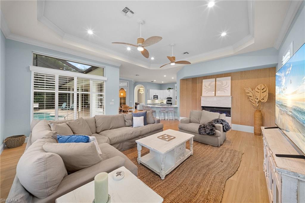 Expansive living area featuring wood-finish flooring, a contemporary fireplace with a decorative wood panel surround, and a vaulted ceiling with recessed lighting