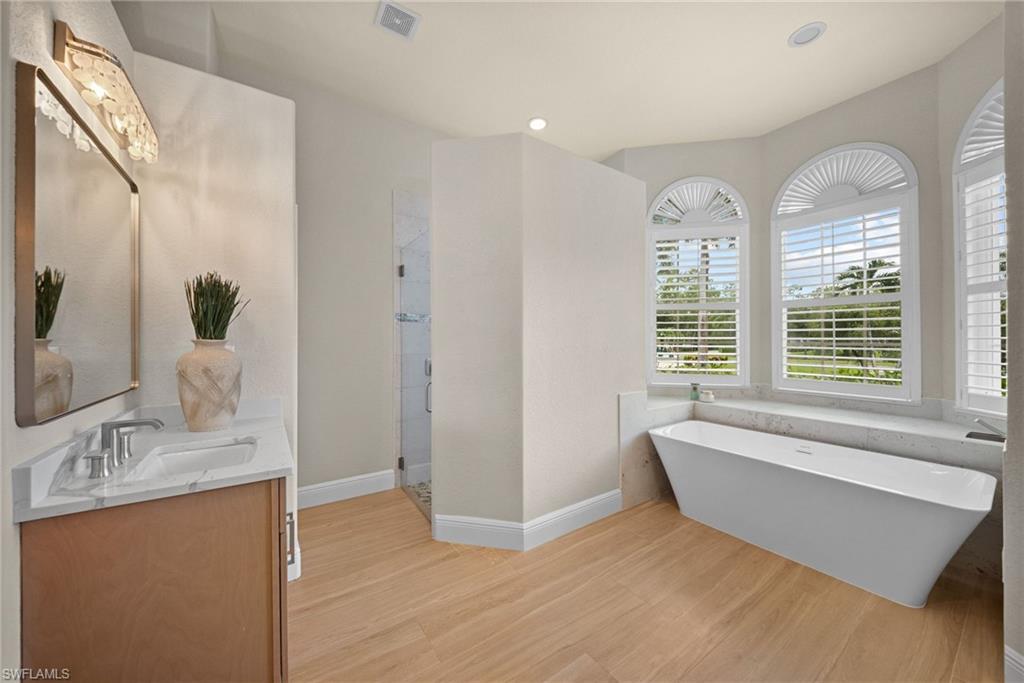 Spacious bathroom featuring a freestanding tub, wood-finish flooring, and arched windows with plantation shutters