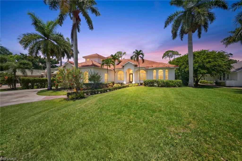 Mediterranean-inspired residence featuring a terracotta tile roof, arched windows, light-toned stucco exterior, mature palm trees, and a manicured front lawn