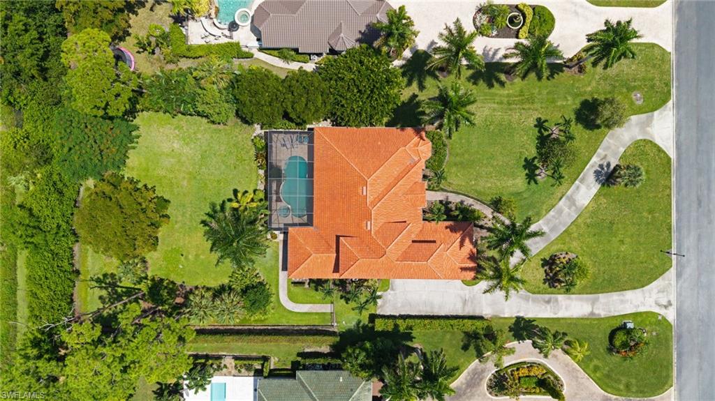 Spanish-style residence featuring a terracotta tile roof, screened pool enclosure, a concrete driveway, and established landscaping with palm trees
