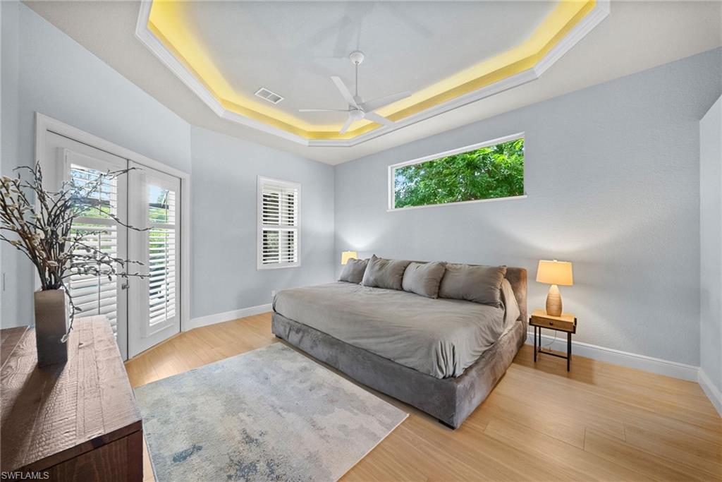 Recessed tray ceiling with accent lighting, light wood-finish flooring, two sets of white louvered French doors, and a horizontal window
