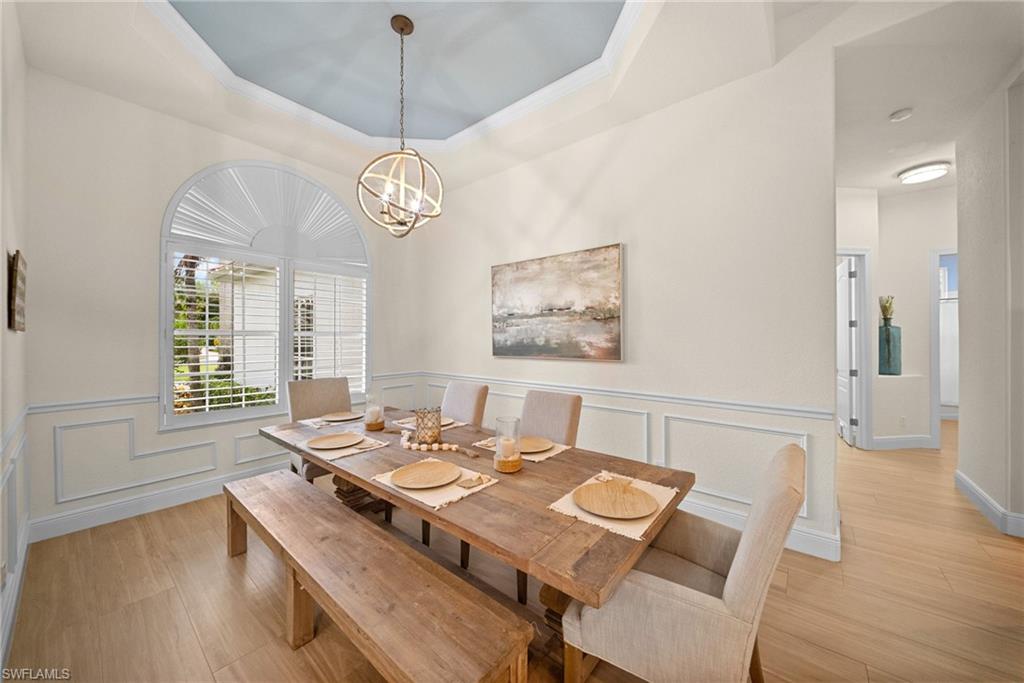 Dining area featuring a tray ceiling with a central chandelier, a large arched window with plantation shutters, and wood-finish flooring