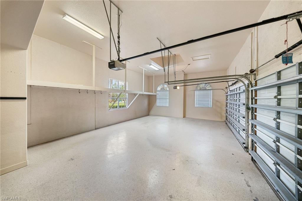Spacious 4 car garage featuring a durable epoxy floor, integrated overhead storage, two arched windows with blinds, and an automatic garage door opener system